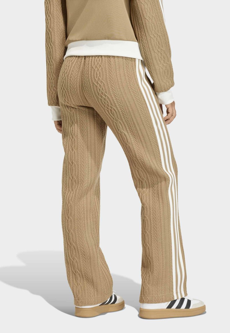 Knit brown athletic pants with cable pattern, white side stripes, and contrasting ribbed cuffs. Paired with white shoes featuring black stripes.