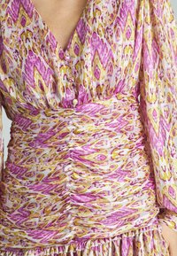 Vestido multicolorido con un patrón abstracto en rosa y amarillo, que presenta un escote en V profundo, cintura fruncida y mangas largas fluidas.