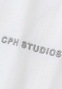 White fabric showing "CPH STUDIOS" in embossed grey embroidery. Smooth texture, clear lettering, no additional patterns or accents.