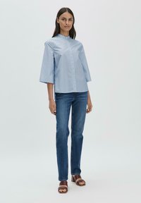 Blusa collared a righe blu e bianche con maniche a tre quarti, abbinata a jeans skinny blu scuro e sandali con tacco blocco marroni.
