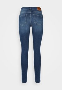 Jeans ajustados en denim azul oscuro. Cuenta con un diseño clásico de cinco bolsillos, detalles de costura y una etiqueta de cuero marrón en la cinturilla.