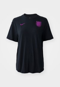 Czarny T-shirt z krótkim rękawem wykonany z miękkiego materiału. Na piersi znajduje się fioletowe logo Nike oraz herb z trzema lwami. Prosty krój.