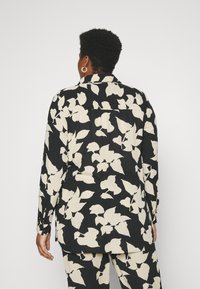 Camicia nera sovradimensionata con motivo di foglie bianche, dotata di colletto, maniche lunghe e orlo dritto, realizzata in tessuto leggero.