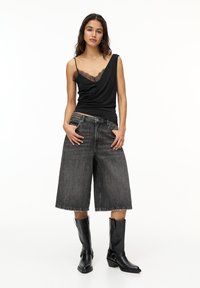 Black sleeveless top with lace trim, paired with dark denim culottes and black heeled boots, showcasing a loose fit and frayed hem.