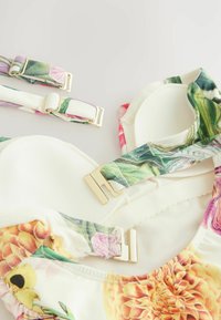 Bra con motivo floreale, con spalline regolabili, hardware dorato e morbido tessuto crema. Presenta colori vivaci e intricati disegni di fiori.