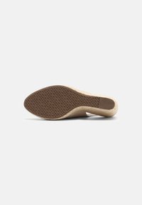 Scarpa con tacco beige con suola testurizzata e parte superiore liscia. La suola presenta un motivo a diamante per maggiore aderenza.