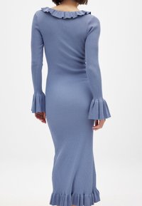 Geripptes blaues langes Kleid mit langen Ärmeln, Rüschenausschnitt und ausladenden Ärmeln. Der Stoff hat eine glatte Textur und eine figurbetonte Silhouette.