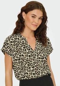 Blus med leopardtryck, kortärmad, v-urringning, i beige och svart färg, lättviktsmaterial och avslappnad passform. Bärs med svarta byxor.