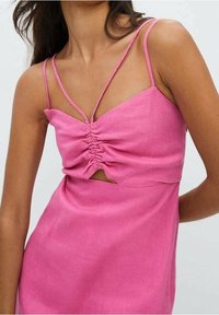 Vestido rosa de lino con tirantes finos, con detalle fruncido en el busto y una sección recortada en la parte delantera. Textura suave con silueta ajustada.