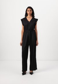 Combinaison noire avec des manches courtes à volants, devant boutonné, ceinture à la taille et jambes larges. Tissu lisse avec une finition polie.