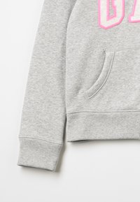 Grå hettegenser med ribbede cuffs og hem, med en frontlomme og fete rosa trykte bokstaver på brystet. Mykt, teksturert stoff.