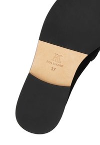Suela de zapato de cuero negro con una superficie lisa. Presenta grabado "CUERO REAL" y tamaño "37" en color marrón claro.