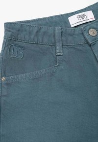 Blauwgroene spijkerbroek met een gestikt logo op het voorvak, een metalen knoop en een standaard taillebandontwerp.