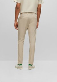 Beiga byxor med slim fit, som har en jämn textur, två bakfickor och förstärkta knäpaneler, i kombination med vita och gröna sneakers.