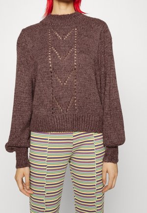 Brauner gestrickter Pullover mit hohem Kragen, der auf der Vorderseite ein pfeilförmiges Ausschnittmuster sowie gerippte Bündchen und Saum aufweist.