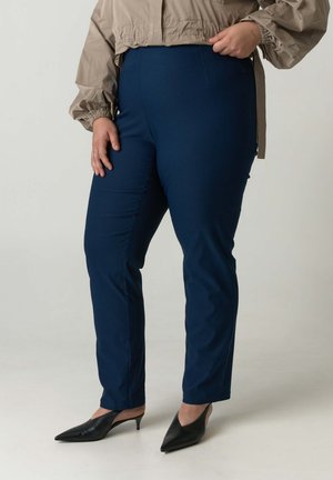 Marineblaue Slim-Fit-Hosen aus glattem, elastischem Stoff, mit hoher Taille und schlanker Silhouette, kombiniert mit schwarzen spitzen Absätzen.