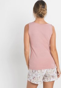 Haut sans manches rose clair avec un col rond, associé à des shorts blancs ornés d'un imprimé floral aux couleurs pastels. Texture de tissu lisse.