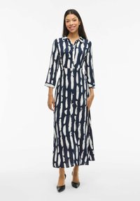 Ilga tamsiai mėlyna suknelė su baltais šepetėlio raštais, mygtukų uždarymu, apykakle ir trijų ketvirčių rankovėmis. Lygus audinys; prigludusi juosmens dalis, platėjanti sijonas.