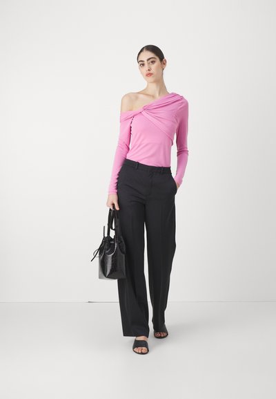 Haut rose clair à manches longues avec un design asymétrique, associé à un pantalon noir taille haute. Les accessoires incluent un sac à main noir et des sandales plates.