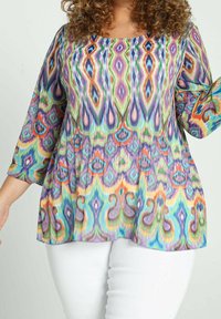 Blouse multicolore avec un motif abstrait vibrant en nuances de violet, vert et orange. Tissu léger, coupe ample, manches trois-quarts.