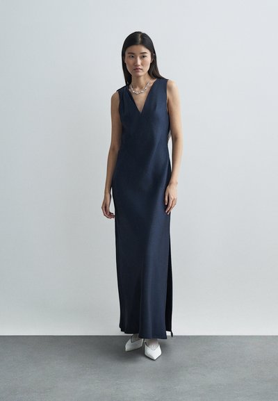 Ναυτικό σατέν μάξι φόρεμα με βαθύ V-ντεκολτέ, που διαθέτει πλαϊνό σκίσιμο. Συνδυασμένο με λευκά μυτερά παπούτσια και κολιέ με μαργαρίτες.