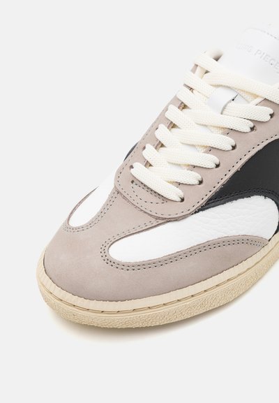 Gray and white sneaker with textured suede and leather, featuring beige rubber sole, round toe, and cream laces. Black accent on the side.