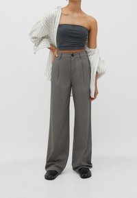 Szare spodnie szerokie w nogawkach z wysokim stanem i fałdami z przodu, w połączeniu z szarym topem bez ramiączek i luźną koszulą w paski. Czarny model slip-on.