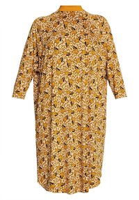 Dlouhé, volné šaty s vysokým výstřihem. Žlutá látka s květinovým a zvířecím vzorem, s černými akcenty a rukávy střední délky.