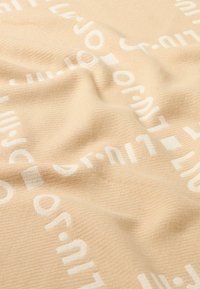 Tessuto beige con un motivo testurizzato che presenta grandi lettere e forme bianche, creando un design moderno e sottile.