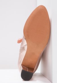 Suola di una scarpa punta metallica rosa con tacco in gomma testurizzata e marcatura taglia 37, posizionata contro pareti bianche.