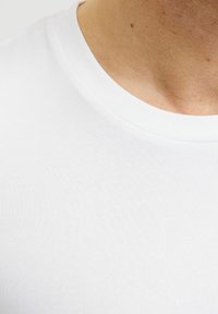 T-shirt blanc en coton avec un col rond, texture lisse et design à manches courtes, présenté en gros plan autour de la zone du cou.