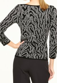Pull noir avec motif abstrait argenté, manches 3/4, coupe ajustée, poignets côtelés, texture douce et encolure arrondie.