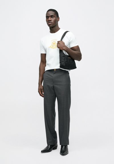 Hvid T-shirt med et gyldent Versace-logo, grå skræddersyede bukser, sort quiltet taske og spidse sorte sko. Simpelt, moderne look.