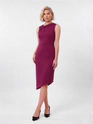 Kobieta o krótkich blond włosach, ubrana w ciemnoróżową sukienkę bez rękawów z asymetrycznym dołem oraz czarne czółenka z ostrym noskiem, stojąca na jednolitym tle.