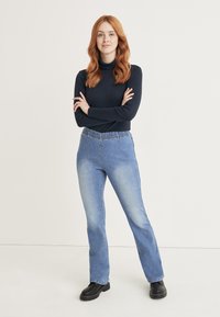 Blå denim flare jeans med elastisk midja, med blekta områden och en mjuk textur, kombinerade med en svart polotröja.
