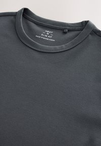 Dunkelgraues, geripptes Slim-Fit-Hemd mit Rundhalsausschnitt, Größe Medium, mit der Aufschrift „Made in Bangladesh“ auf dem Innenkragen.