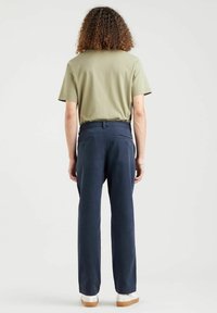 Granatowe spodnie o prostym kroju, z fakturowanej tkaniny, z tylnymi kieszeniami; zestawione z oliwkowozielonym t-shirtem z krótkim rękawem i jasnymi trampkami.