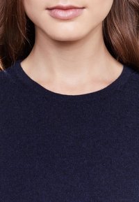 Námořnicky modrý pletený svetr s kulatým výstřihem. Hladká textura a jednotný vzor, zdůrazňující měkkost a teplo materiálu.