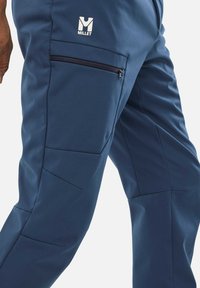 Pantalons de randonnée bleu marine en tissu durable, avec une poche zippée, des coutures angulaires et un logo Millet à l'avant.