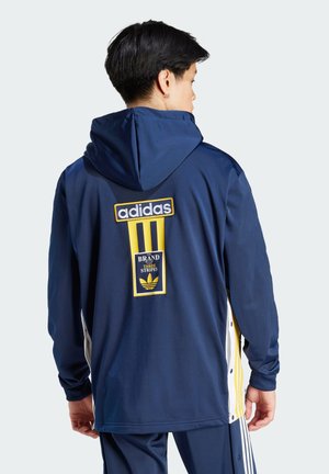 Marina huva sweatshirt med gula detaljer, med Adidas-logotyp och en rektangulär logotyp på baksidan. Slät tyg; avslappnad passform.