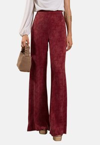 Pantalons amples bordeaux en tissu doux avec un motif subtil. Associés à un haut blanc et un sac à main en cuir texturé marron.