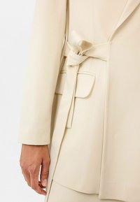 Beige op maat gemaakte blazer met een zijsluiting, een gladde textuur en een enkele zak. Stijlvolle revers maken het gestructureerde ontwerp compleet.
