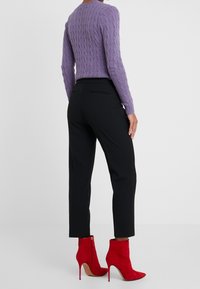 Lila kabelstickad tröja, svarta skräddarsydda byxor och röda mocka ankelskor med hög klack och sidoblixtlås.