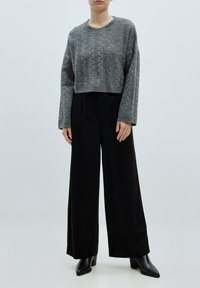Grijze kabelbrei cropped trui met lange mouwen, gecombineerd met zwarte high-waisted wijde broek en zwarte blokhakken.