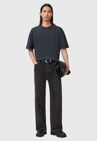 Ciemnoszary, oversize t-shirt z krótkim rękawem, w połączeniu z prostymi czarnymi dżinsami i czarnymi butami. Trzyma teksturowaną ciemną torbę.