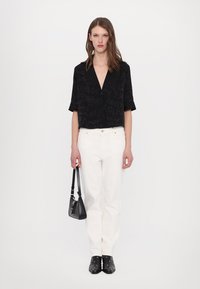 Svart kortärmad blus med subtilt mönster, vita högmidjade jeans, svart handväska och ankelstövlar med silverdetaljer.