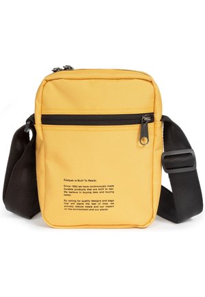 Yellow rectangular crossbody bag with black adjustable strap, front zip pocket, and printed brand sustainability text on the front.