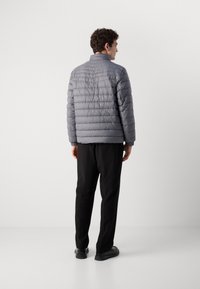 Gray quilted puffer jacket with a standing collar, elastic cuffs, and a slim fit design, paired with black trousers and shoes.