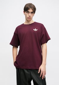 Burgundijas īsā piedurkne T-krekls, izgatavots no kokvilnas, ar baltu logo kreisajā krūtīs un brīvu piegriezumu.