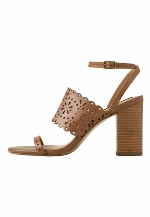 Sandal alto in pelle marrone con design floreale a intaglio, cinturino alla caviglia regolabile e tacco spesso texturizzato. Stile con punta aperta.